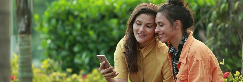Two female friends sitting in a park looking at a mobile phone.