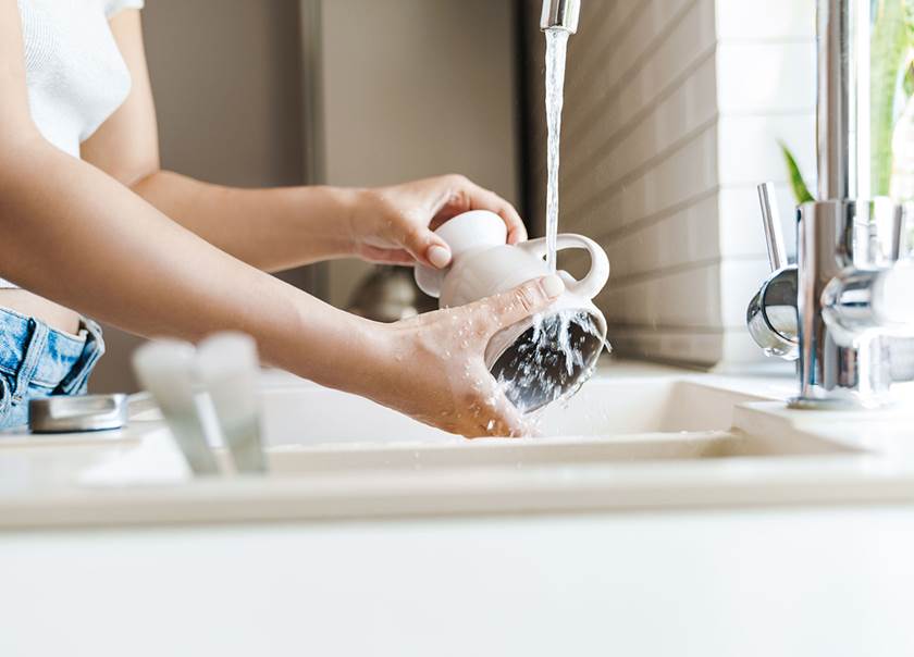 Woman rinsing off a cup under running water in the sink.