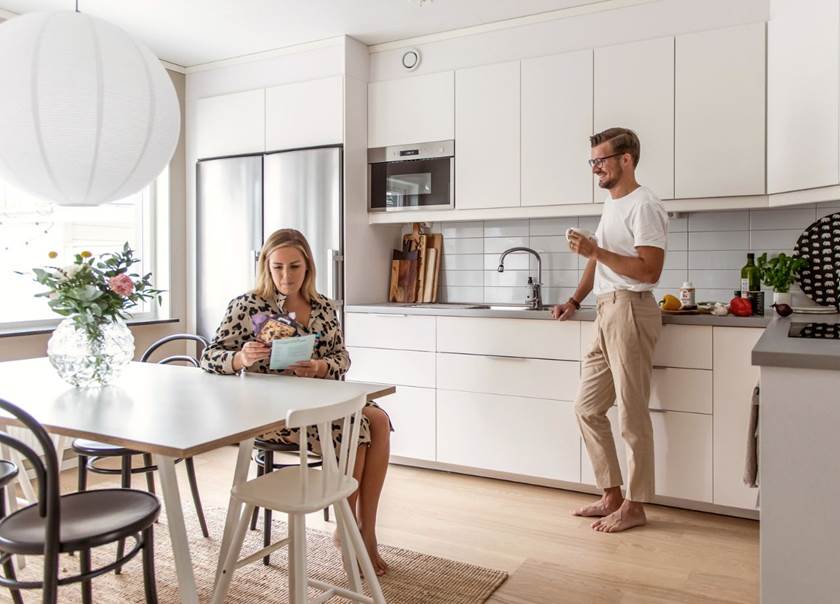 Lady sat at kitchen table and husband stood leaning on work top