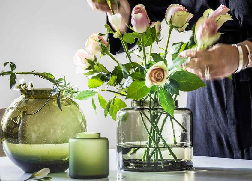 Three vases. Two green vases and one clear vase with flowers