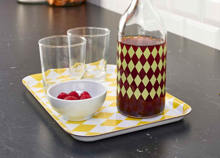 Yellow patterned tray with glass bottle of juice and glasses