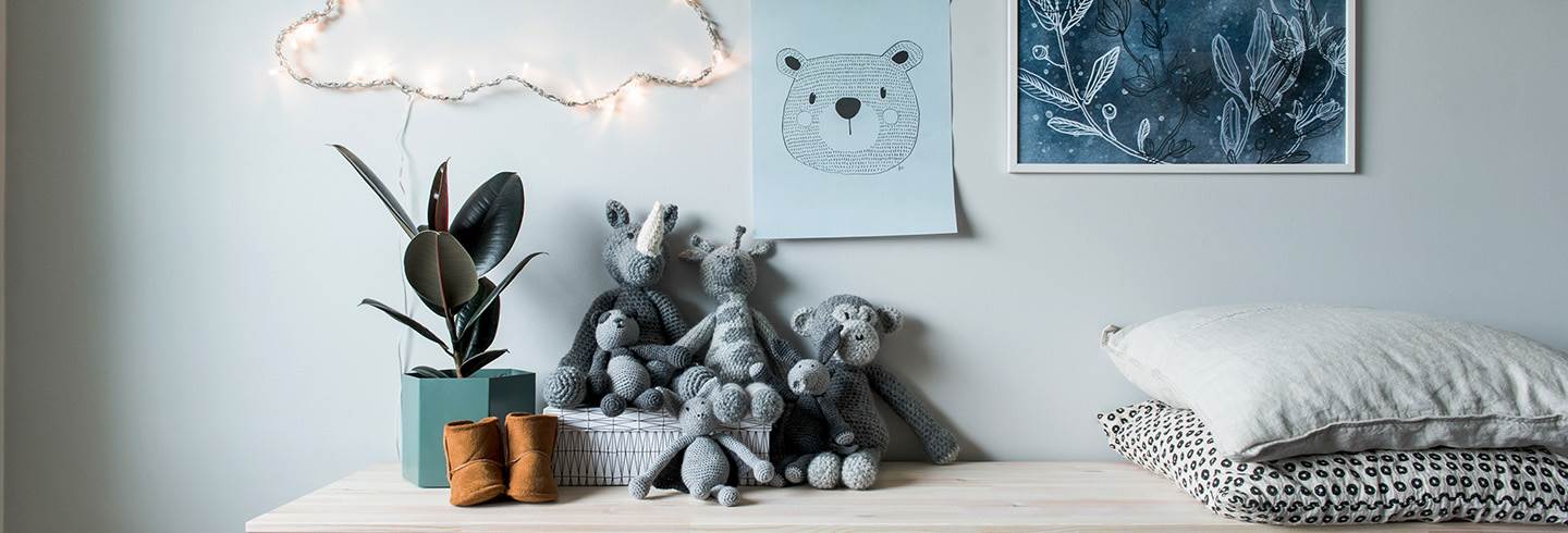 Crocheted teddies, pillows, plant and childrens shoes on dresser with posters over.