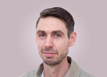 Portrait of a man in brown hair, with a beige shirt.