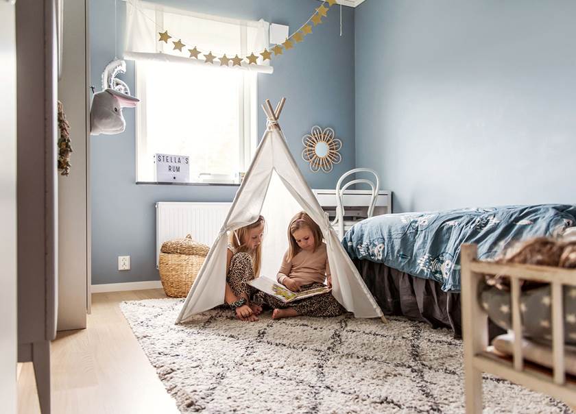 Two girls sitting in a tent in the childrens room and reading a book.